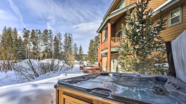 A wooden hot tub with a view of a snow-covered landscape and a building with a balcony. - Winter Park Townhome w/ Hot Tub, Ski Shuttle! (Winter Park)