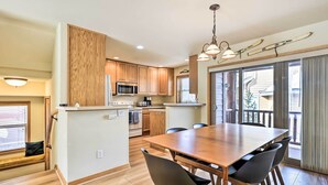 A modern kitchen with wooden cabinets, a central island, and a dining area with a large table and chairs. - Winter Park Townhome w/ Hot Tub, Ski Shuttle! (Winter Park)