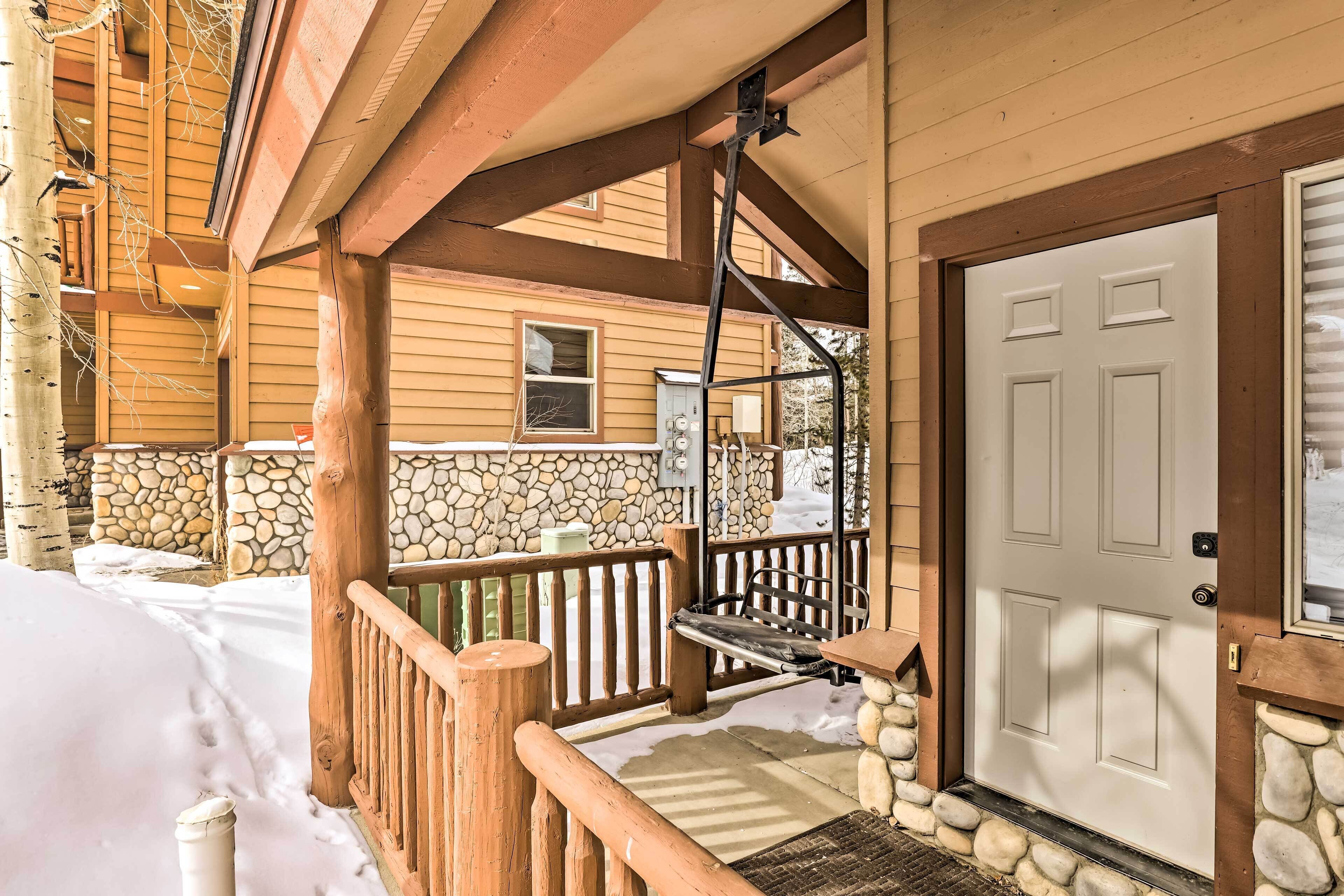 A wooden porch with a stone wall, a white door, and a stone fireplace.