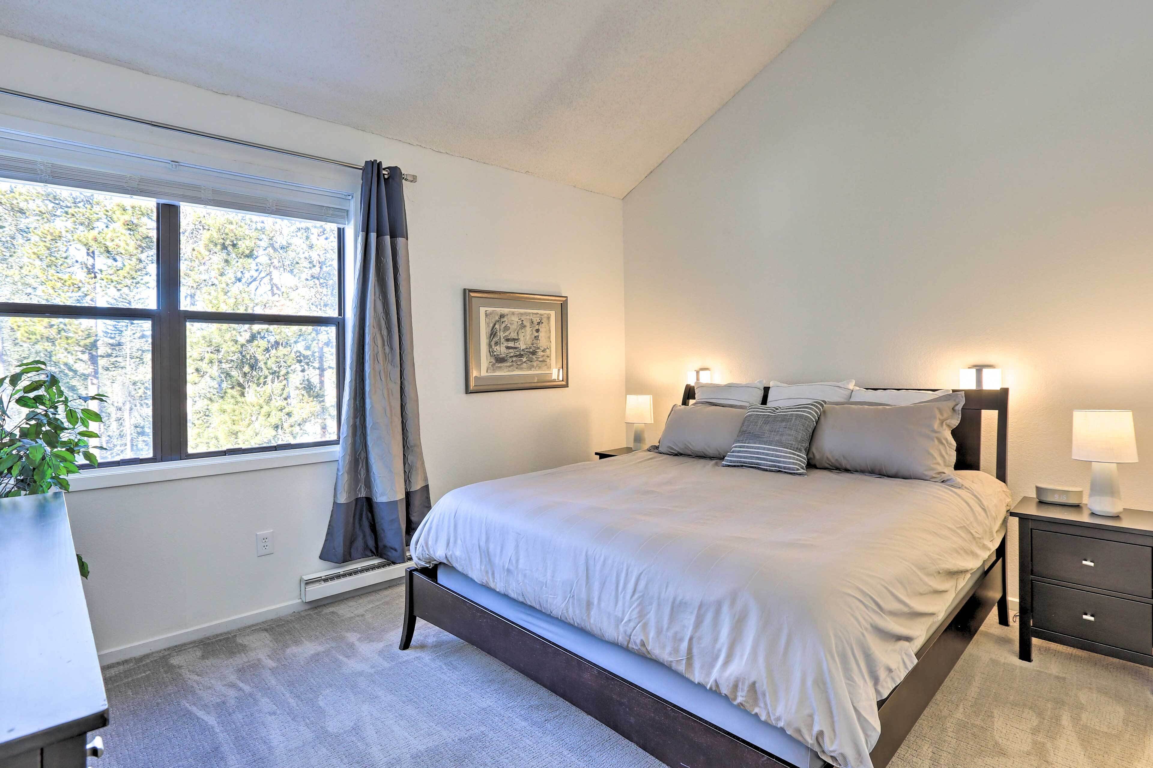 A bedroom with a large bed, bedside tables with lamps, a window with curtains, and a framed picture on the wall.