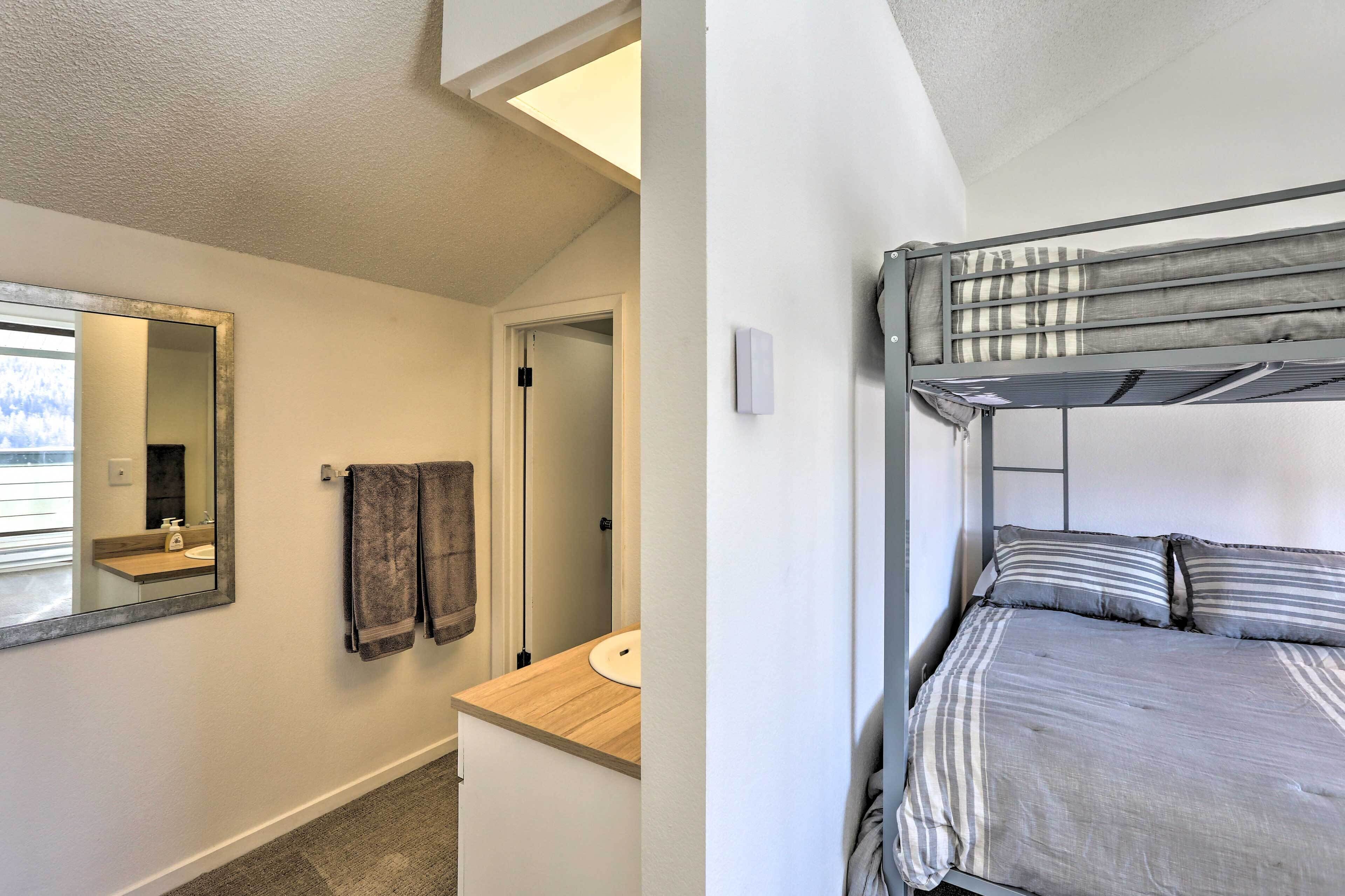 Quarto com uma cama de solteiro e beliche, espelho, pia e porta-toalhas.