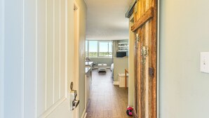 A hallway leading to a bedroom with a window, a wooden door, and a white wall. - PCB Coastal Condo w/ On-site Beach Access! (Panama City Beach)
