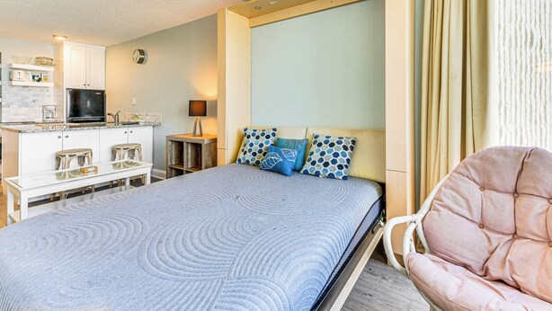 A bedroom with a bed, a chair, a desk, and a kitchenette. - PCB Coastal Condo w/ On-site Beach Access! (Panama City Beach)