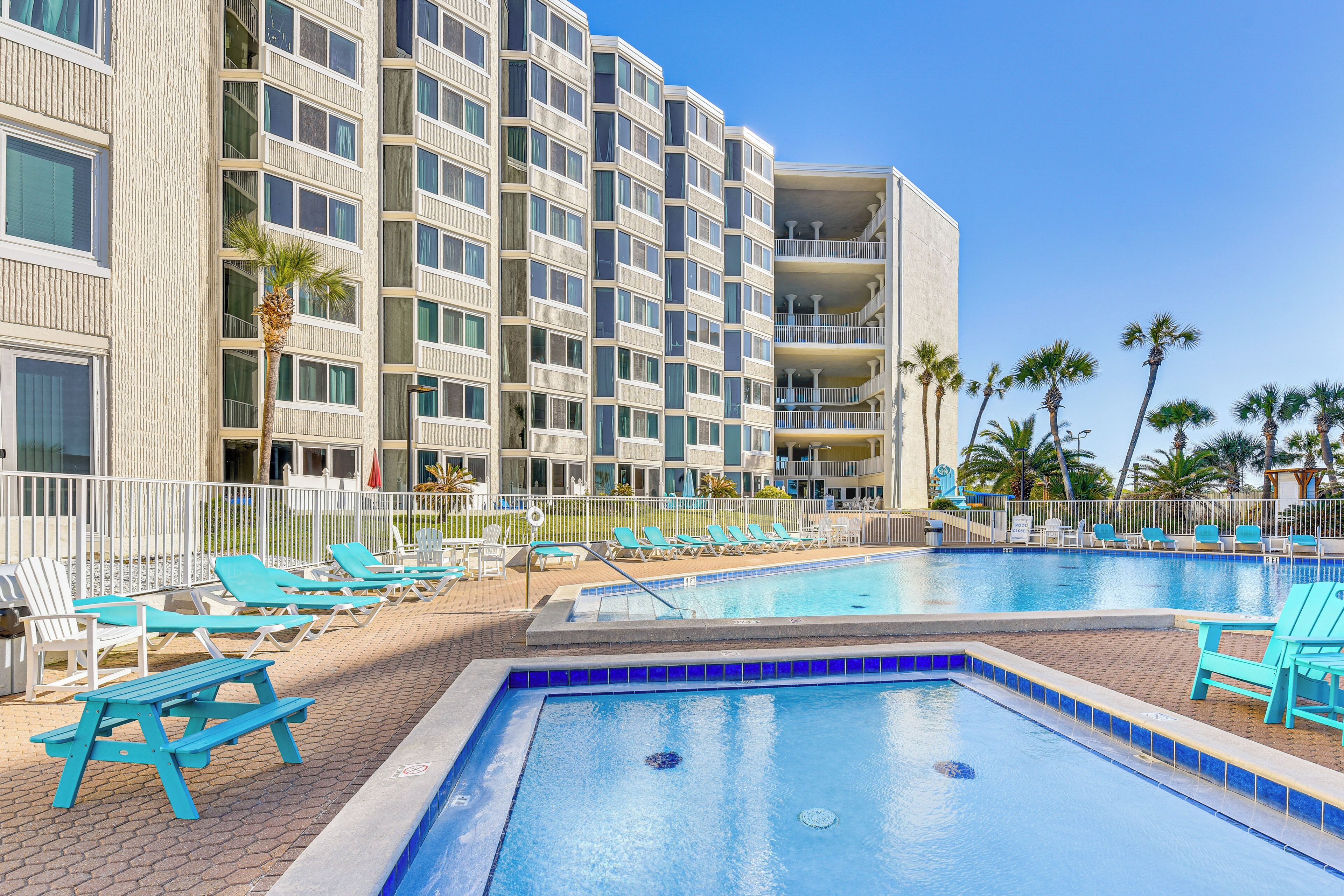 A hotel with a swimming pool, sun loungers, and a view of palm trees.
