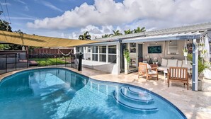 Ein Schwimmbecken mit Sonnenschirm, eine überdachte Terrasse mit Sitzgelegenheiten und Blick auf den Himmel.