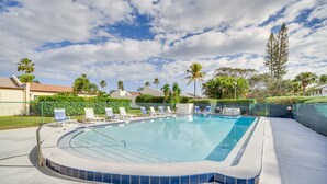 Una piscina con borde de azulejos, rodeada de sillones de descanso y palmeras.