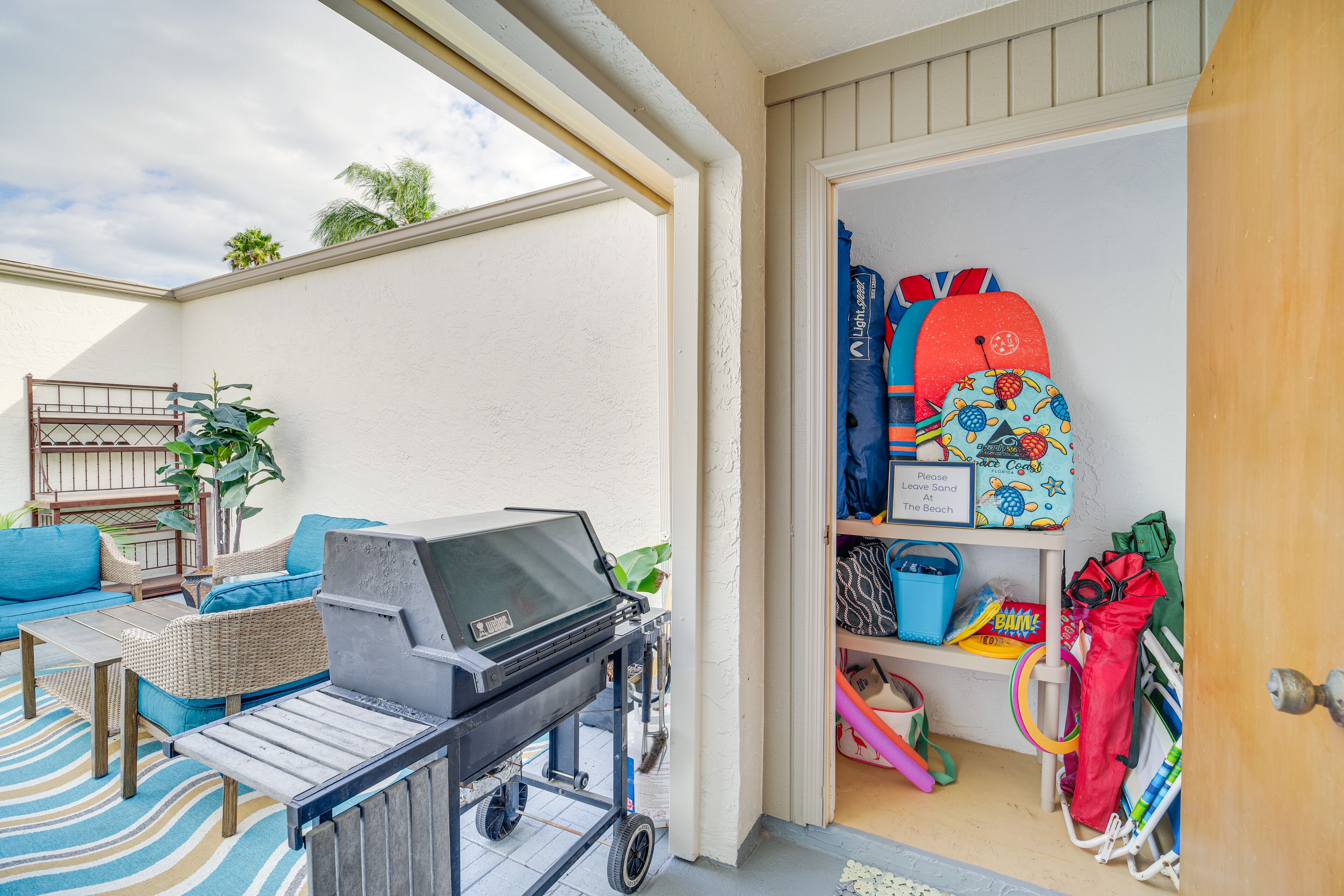 A patio area with a grill, wicker furniture, and a storage shelf with beach gear.