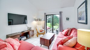 Una sala de estar con un sofá, una mesa de centro, un televisor, una silla y una ventana con cortinas.