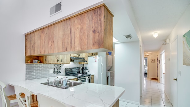 Una cocina moderna con encimeras de mármol blanco, armarios de madera y una isla central con taburetes de bar.