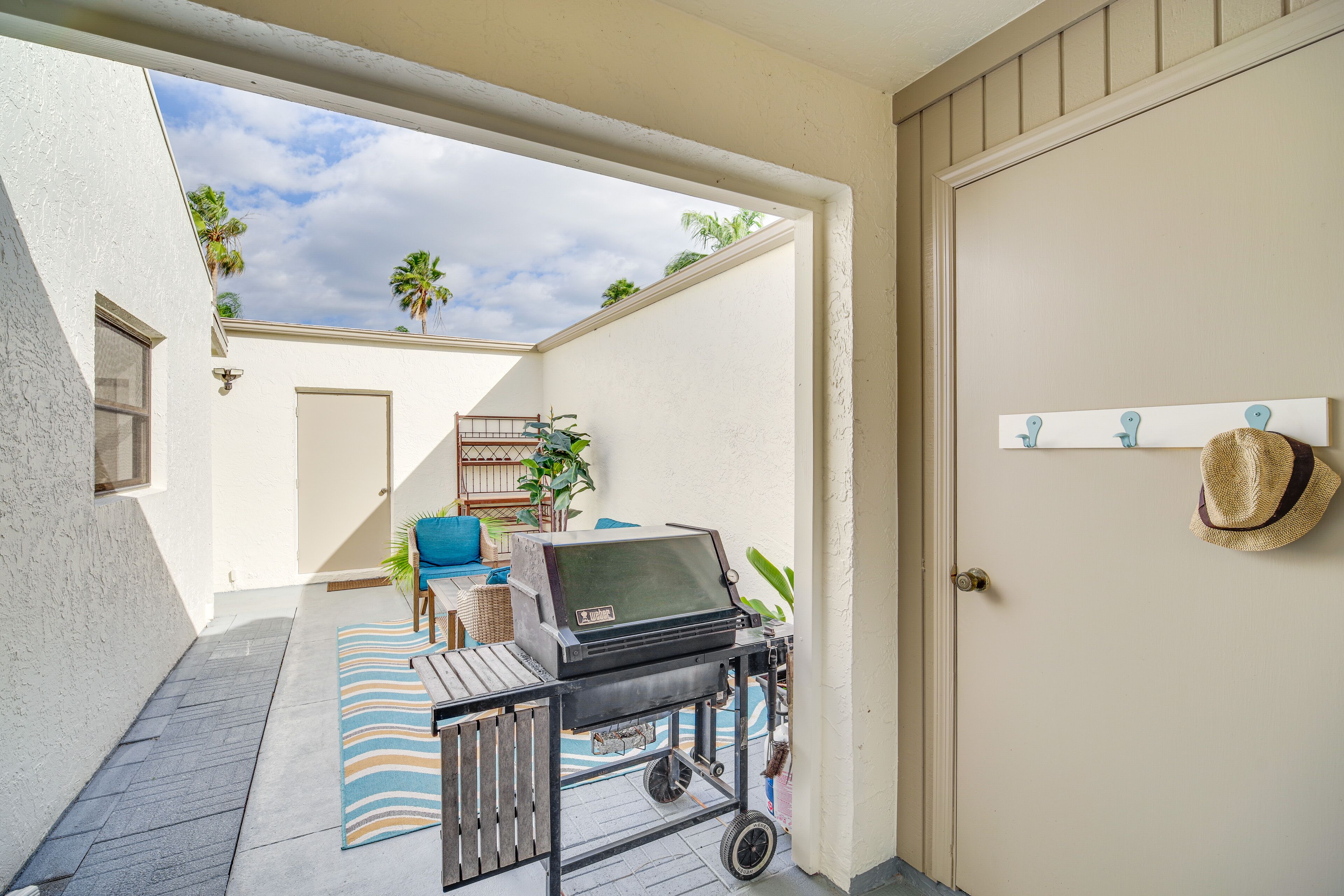 Un patio con una parrilla, una silla azul y un tapete a rayas.