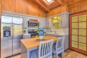Une cuisine avec un lambris en bois, des appareils électroménagers en acier inoxydable, une table à manger en bois avec deux chaises et une plante en pot.