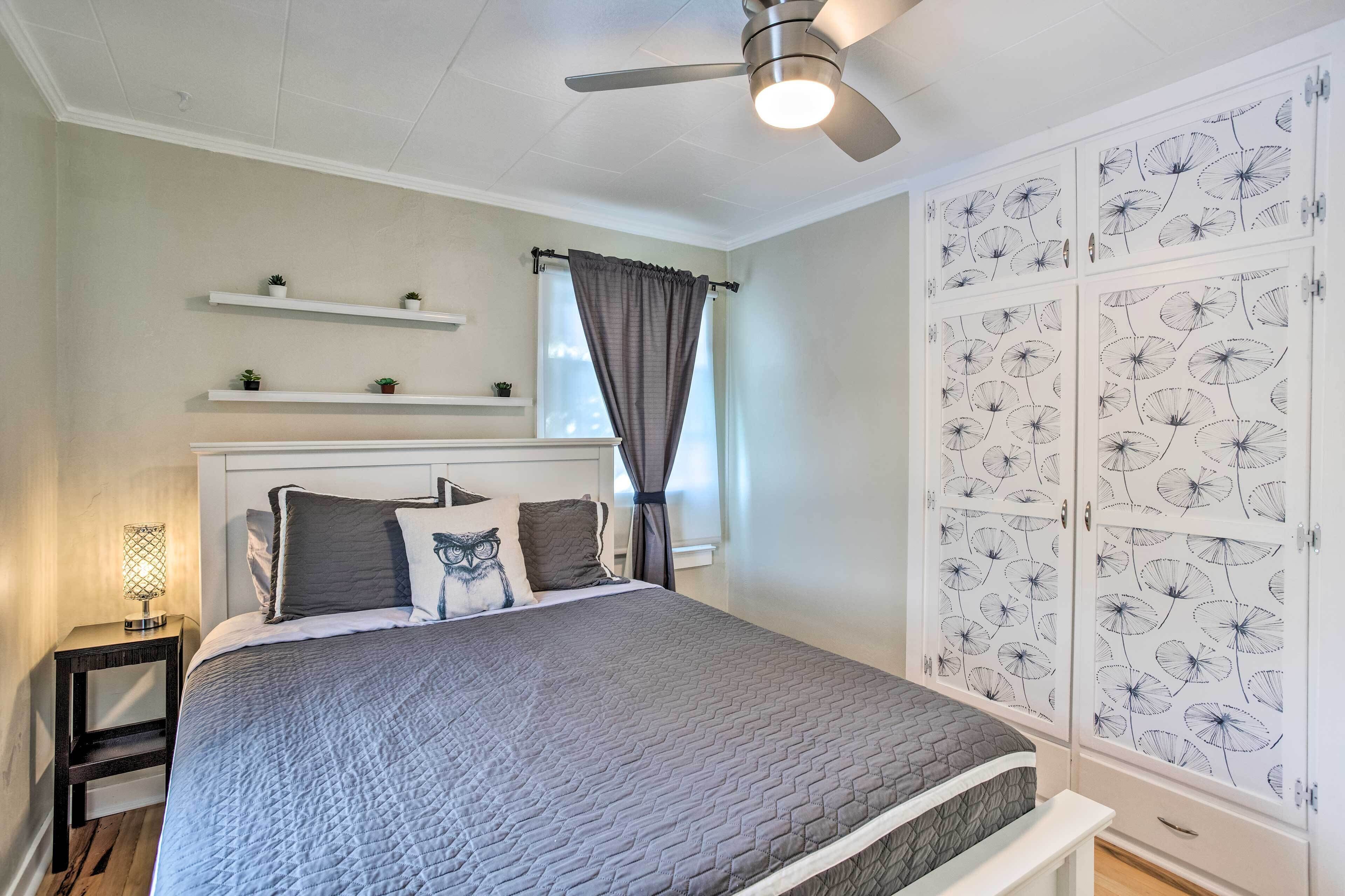 Een slaapkamer met een bed, een nachtkastje, een plafondventilator, een raam met gordijnen, en een garderobe met een bloemenmotief.