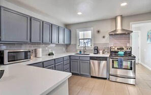 A modern kitchen with grey cabinets, stainless steel appliances, and a white countertop. - Grand Junction Vacation Rental w/ Fire Pit! (Grand Junction)
