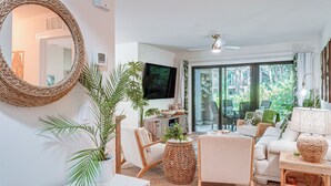 A living room with a large mirror, wicker furniture, a flat-screen TV, and a view of the outdoors.