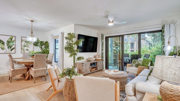 A spacious living room with a dining area, large windows, and a TV.