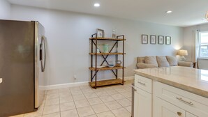 A kitchen with a stainless steel refrigerator, a wooden shelf unit, a beige sofa, and a window with natural light. - < 3 Mi to Juno Beach: Coastal Townhome w/ Patio! (Juno Beach)