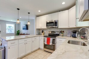A modern kitchen with white cabinets, stainless steel appliances, and pendant lighting.