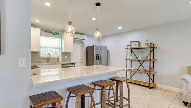 A modern kitchen with a central island, bar stools, pendant lights, and a wooden shelf unit. - < 3 Mi to Juno Beach: Coastal Townhome w/ Patio! (Juno Beach)