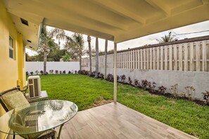 A covered patio with a glass table and wicker chairs, a white fence, and a well-maintained lawn.