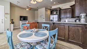 A modern kitchen with dark wood cabinets, a white countertop, and a dining area with blue chairs and a white table.