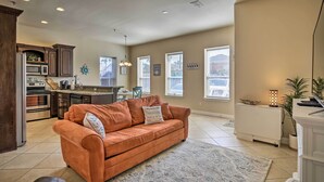 A spacious living room with a large orange sofa, a kitchen area with dark wooden cabinets, and a ceiling fan.