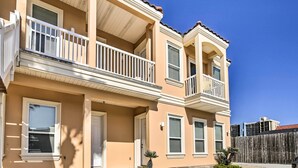 A two-story residential building with a beige exterior, white balconies, and a wooden fence in the background.