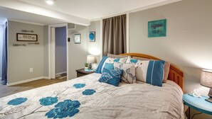 Une chambre à coucher avec un lit, une table de chevet, une lampe et un mur orné d’une affiche et d’un tableau.