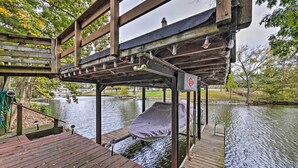 Eine Holzstele führt über ein Gewässer, mit einem Boot unter einem Dach und einer Metallkonstruktion mit Beleuchtung.