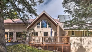 Une maison à deux étages dotée d’une terrasse en bois, de grandes fenêtres et d’un panneau solaire sur le toit.
