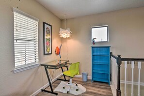 Une pièce avec un bureau en verre, une chaise verte, un tapis blanc, un meuble de rangement bleu et un radiateur blanc.