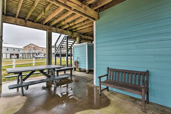 Un espace pique-nique abrité, avec des bancs et des tables en bois, un mur bleu et une vue sur un bâtiment en arrière-plan.