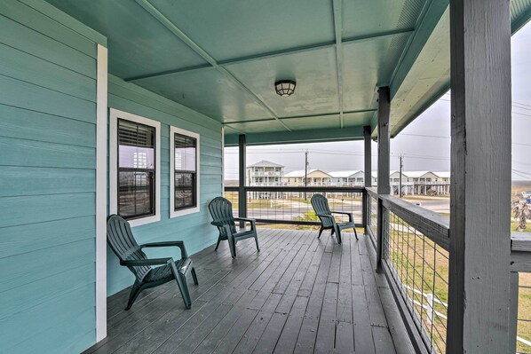 Une véranda couverte avec deux fauteuils Adirondack, une balustrade et une vue sur les maisons au loin.
