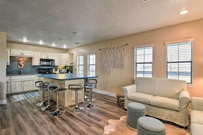 A modern kitchen with white cabinets, a central island with bar stools, and a dining area with a sofa and ottoman. - Idyllic Gulf Coast Escape: Steps to Surfside Beach (Freeport)