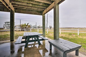 A wooden picnic table under a covered area with a view of houses and a fence in the background. - Idyllic Gulf Coast Escape: Steps to Surfside Beach (Freeport)