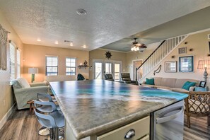 A spacious kitchen with a central island, a dining area with bar stools, a staircase, and a living area with a sofa and decorative wall art. - Idyllic Gulf Coast Escape: Steps to Surfside Beach (Freeport)