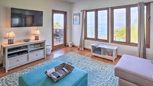 A living room with a TV, two lamps, a sofa, a coffee table, and a view of the sea through large windows. - Quiet Avalon Getaway Villa w/ Ocean View & Balcony (Avalon)