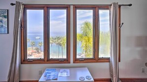 A room with three large windows, a white table with papers, and a view of the sea and palm trees. - Quiet Avalon Getaway Villa w/ Ocean View & Balcony (Avalon)