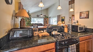 A modern kitchen with a built-in oven, microwave, and gas stove. There are hanging pendant lights, a clock on the wall, and a window providing natural light. - 3 Mi to Skiing: Big Bear Cabin w/ Deck (Big Bear City)
