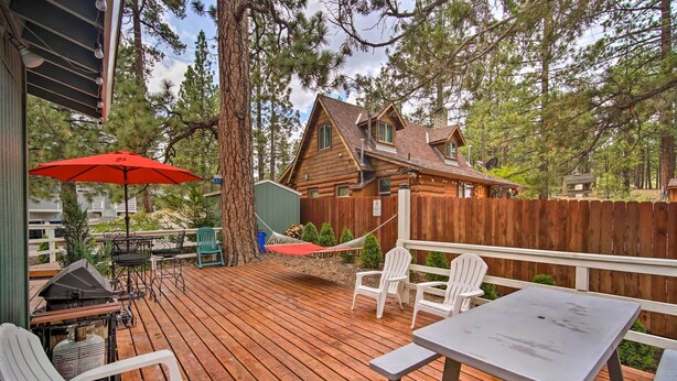 A wooden deck with outdoor furniture, a hammock, and a view of a cabin surrounded by trees. - 3 Mi to Skiing: Big Bear Cabin w/ Deck (Big Bear City)
