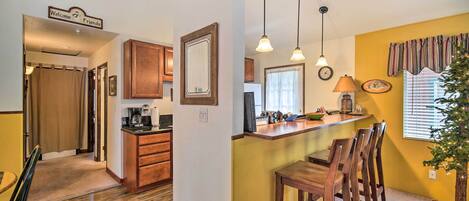 Una cocina con armarios de madera, cafetera y zona de comedor con sillas de madera y una mesa pequeña.