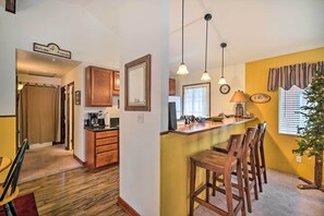 A kitchen with wooden cabinets, a coffee maker, and a dining area with a bar counter and chairs. - 3 Mi to Skiing: Big Bear Cabin w/ Deck (Big Bear City)