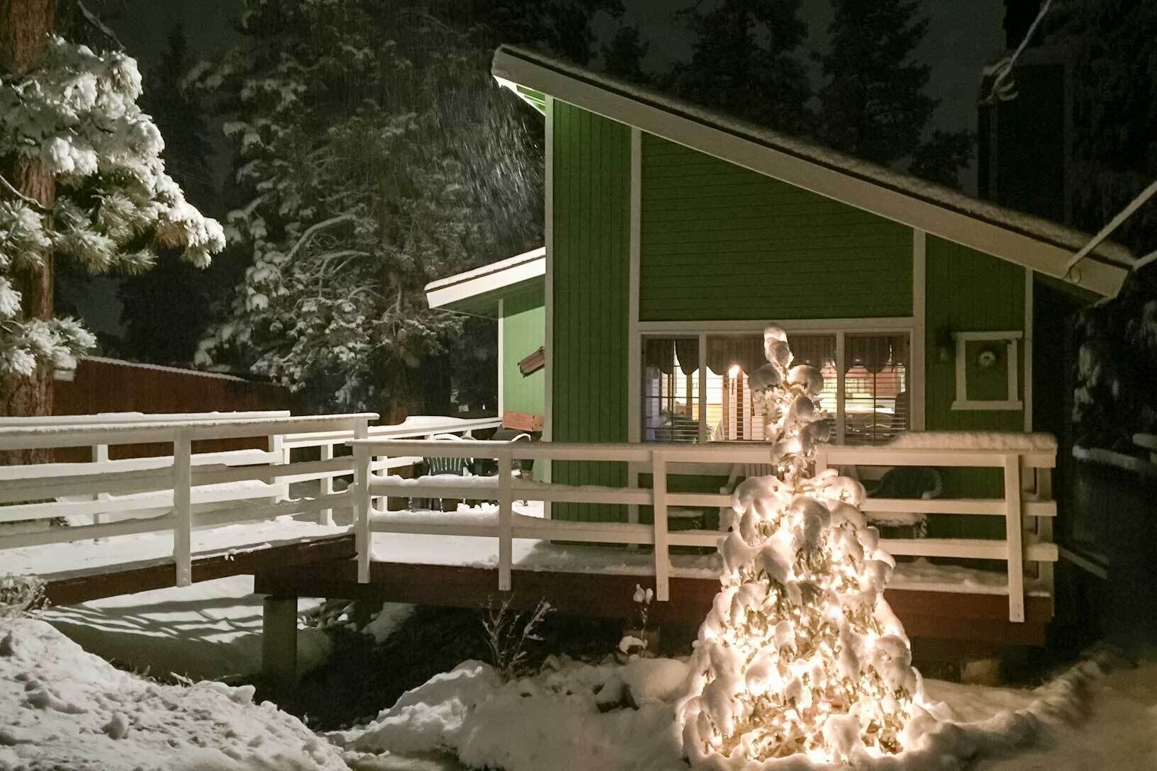 Een groen gebouw met een witte hek, een sneeuw bedekte veranda en een sneeuwbeeld.
