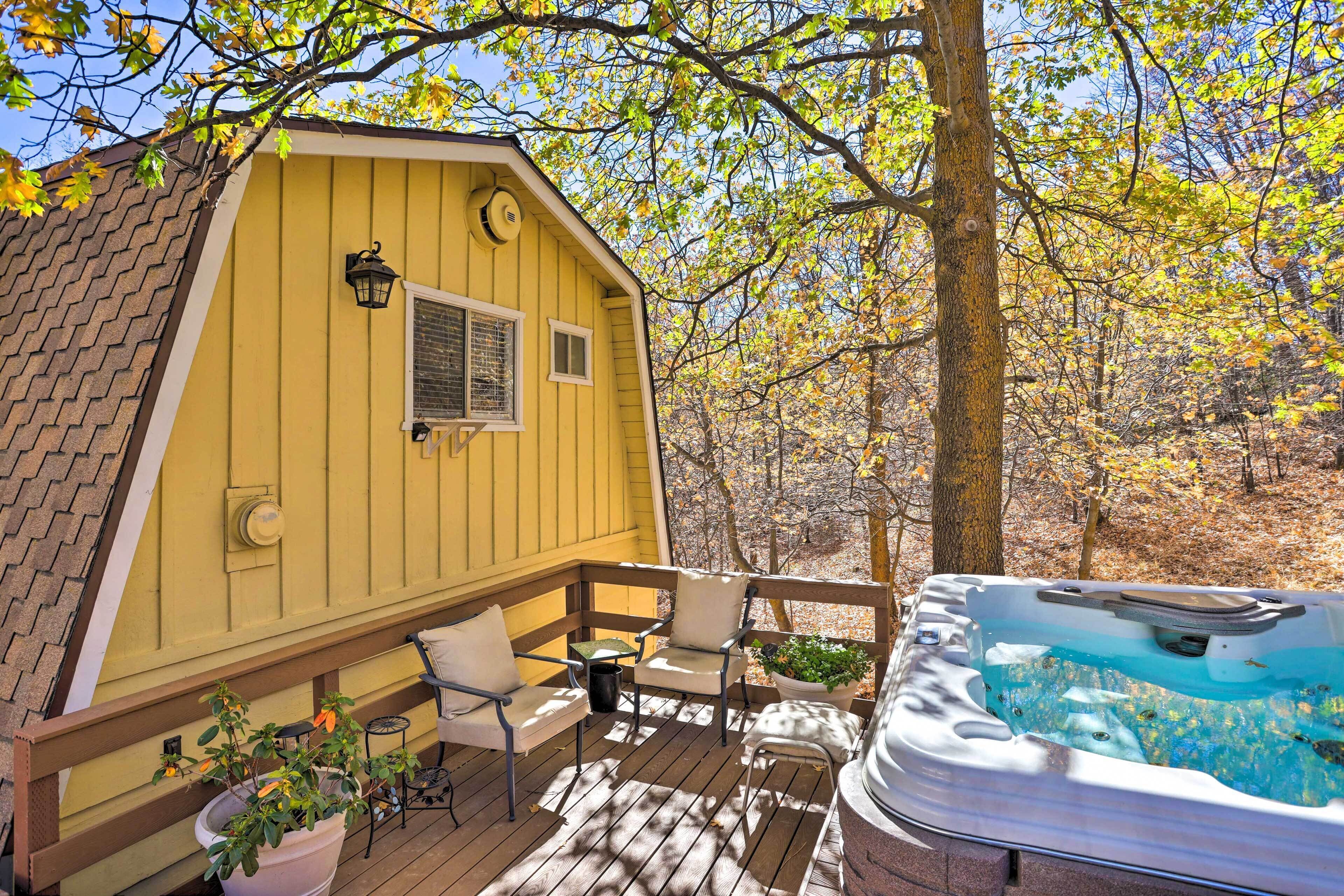 Eine gelbe Holzhütte mit Whirlpool auf einer Holzterrasse, umgeben von Bäumen.