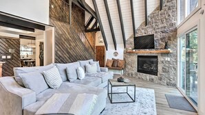 A spacious living area with a stone fireplace, a large sectional sofa, and a modern chandelier. - Luxe Timberland Villa w/ Lake Arrowhead Access! (Lake Arrowhead)