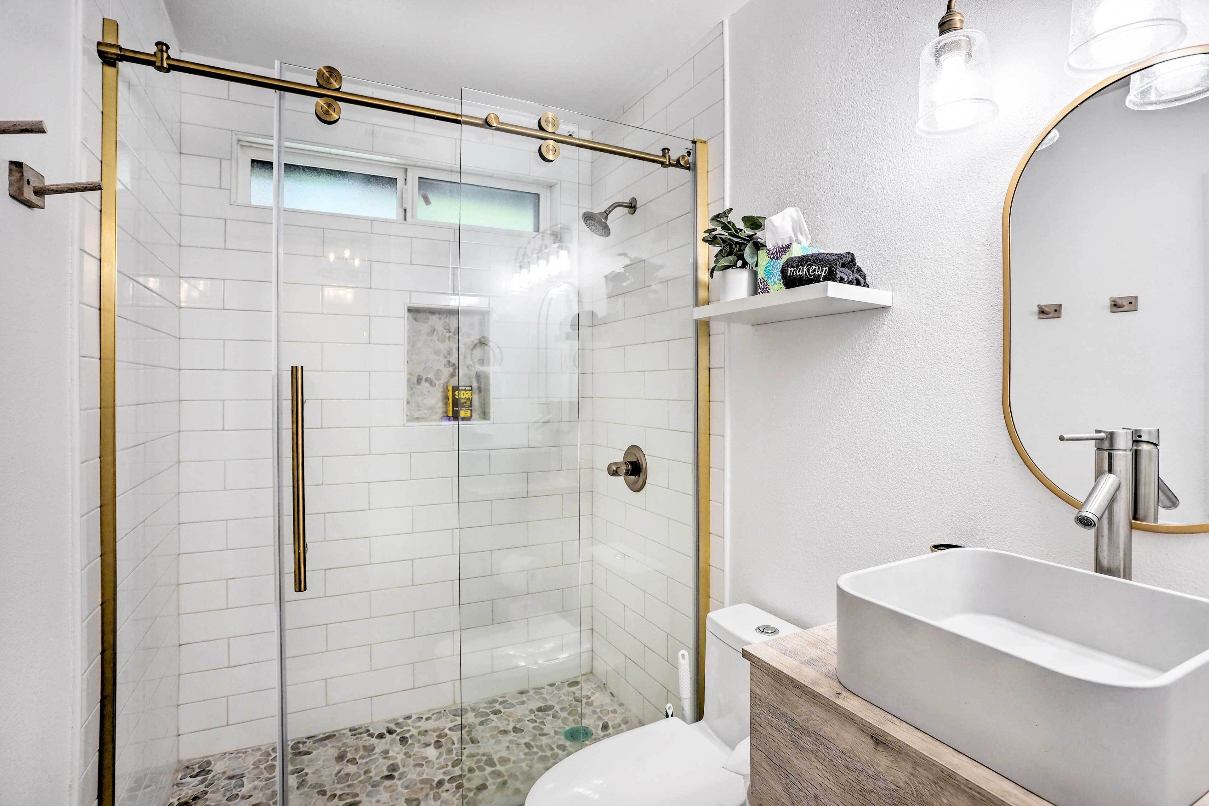 Un baño moderno con ducha envuelta en vidrio, lavabo blanco y tocador de madera.