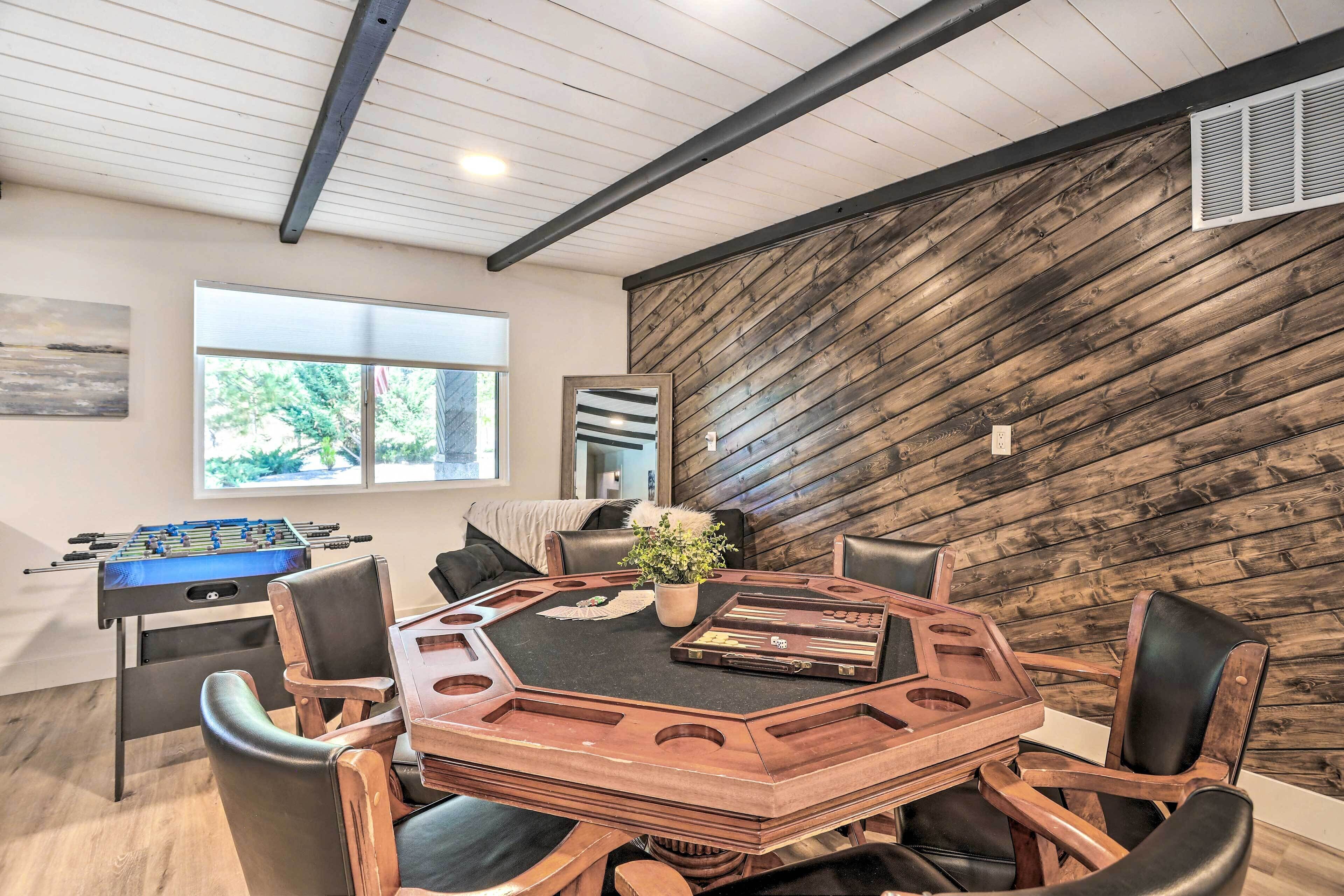 Una habitación con una mesa de madera, sillas, una mesa de futbolín y un ventanal grande.