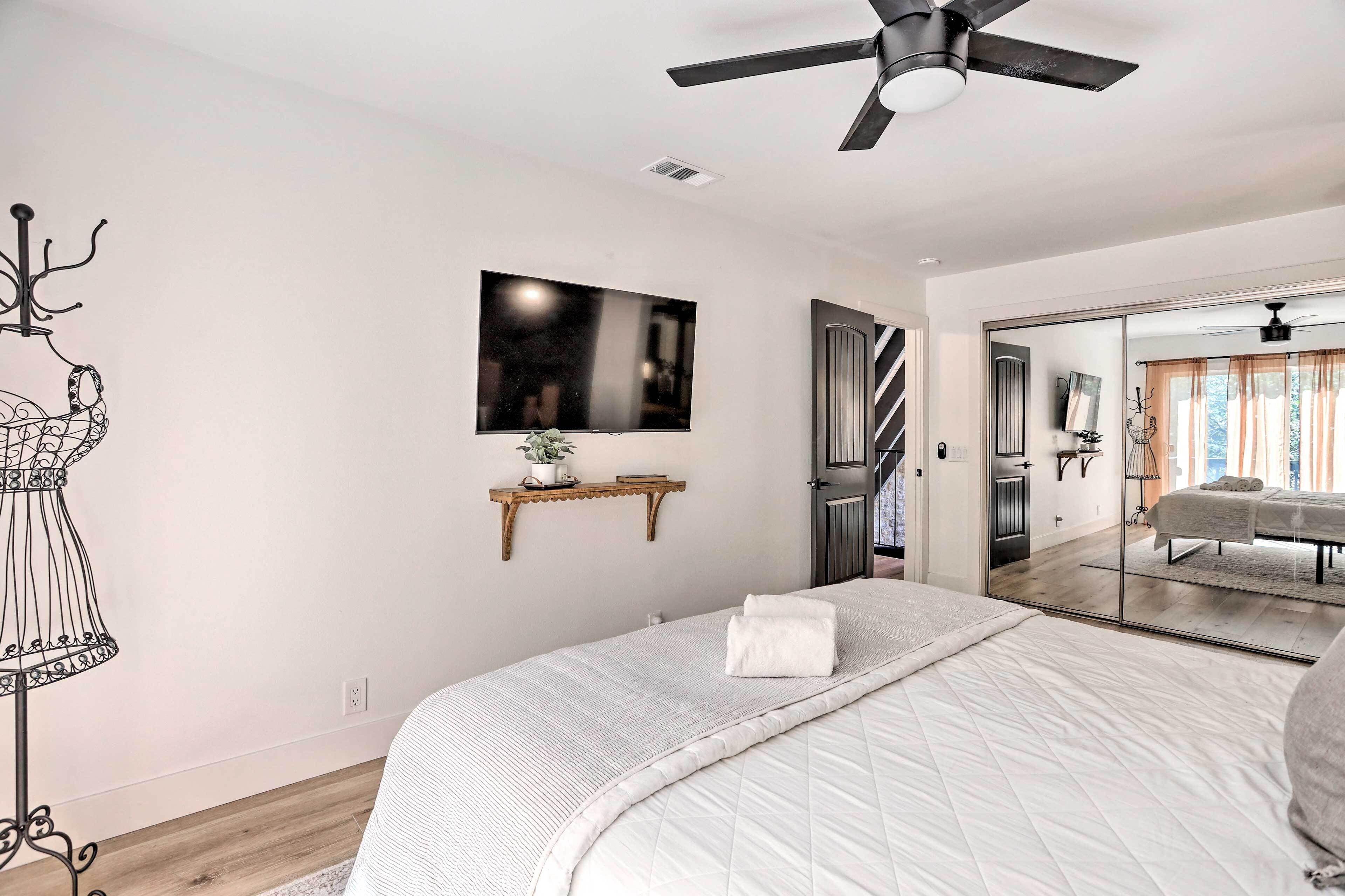 A bedroom with a bed, a ceiling fan, a TV, and a mirror.