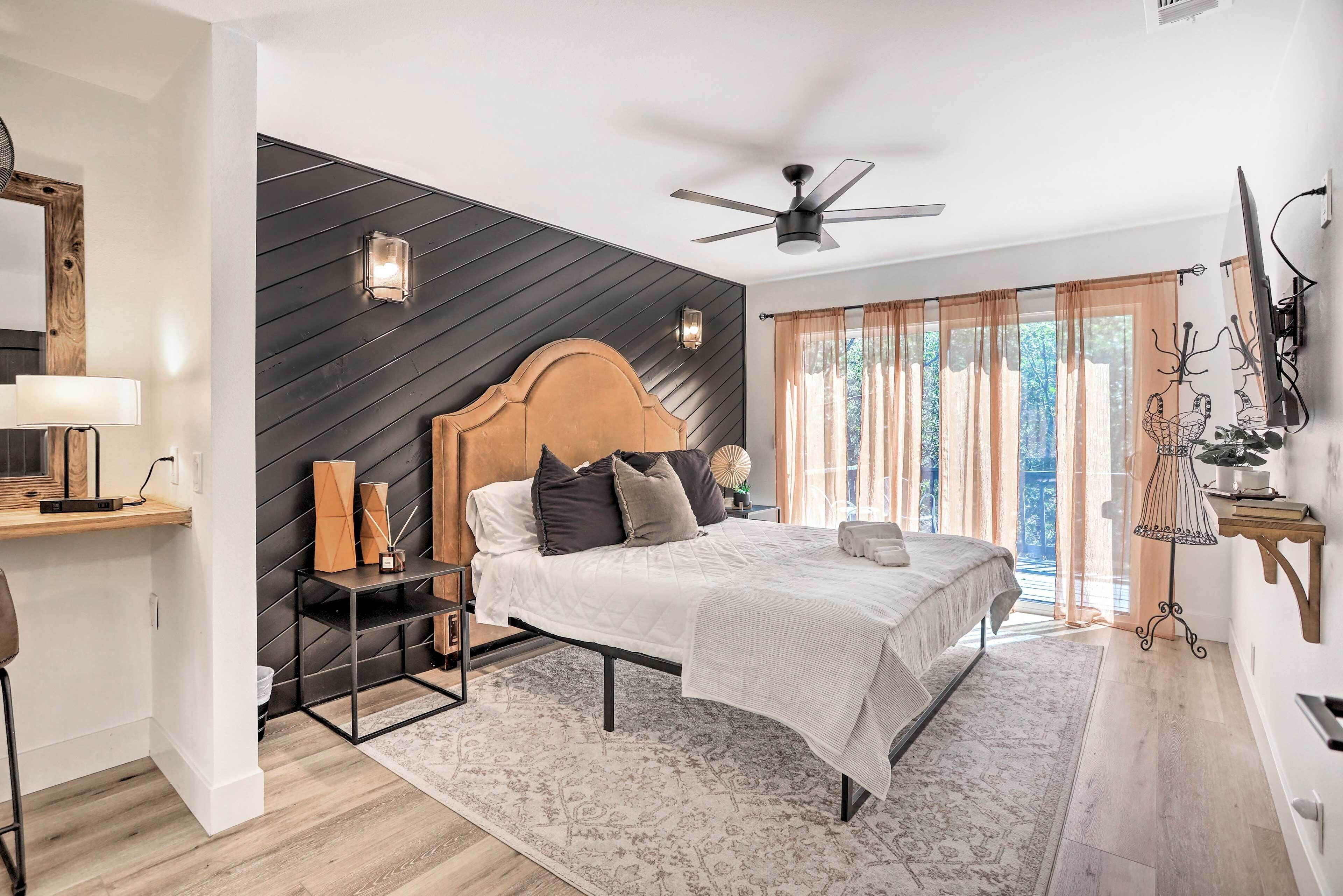 A modern bedroom with a bed, a ceiling fan, a nightstand, a lamp, and a window with curtains.