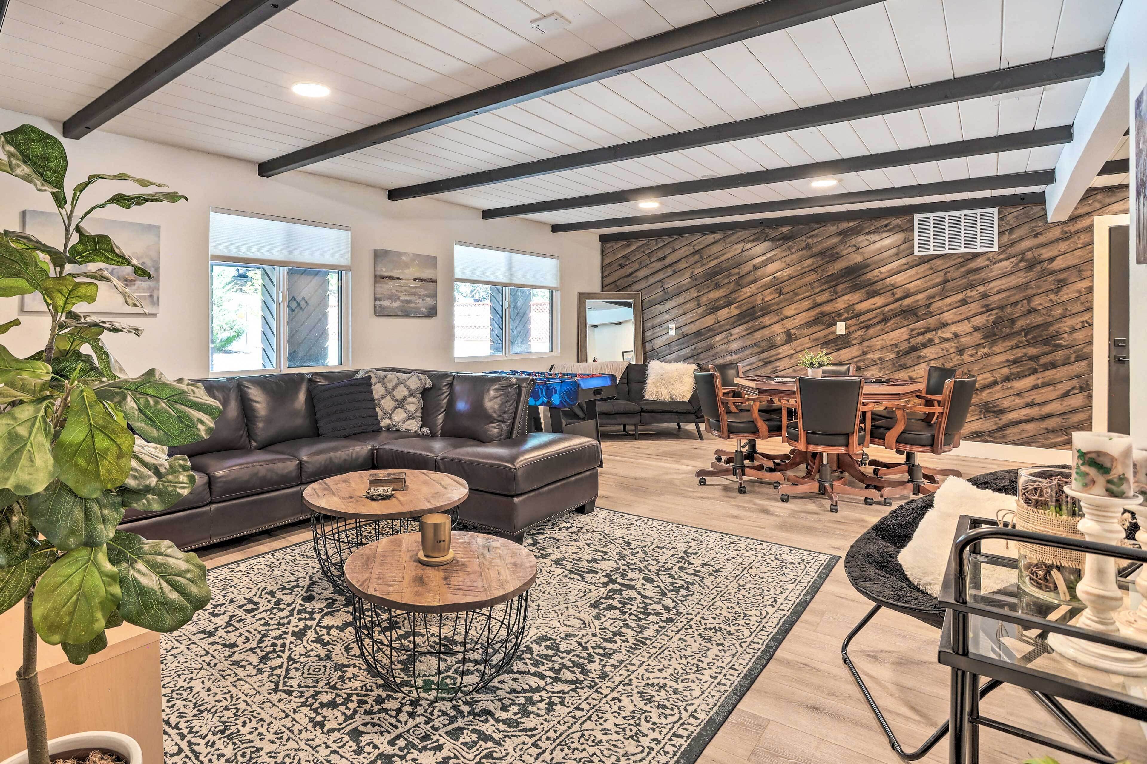 Un salon spacieux avec un canapé en cuir foncé, deux petites tables rondes, un tapis à motifs et un mur décoratif en bois.