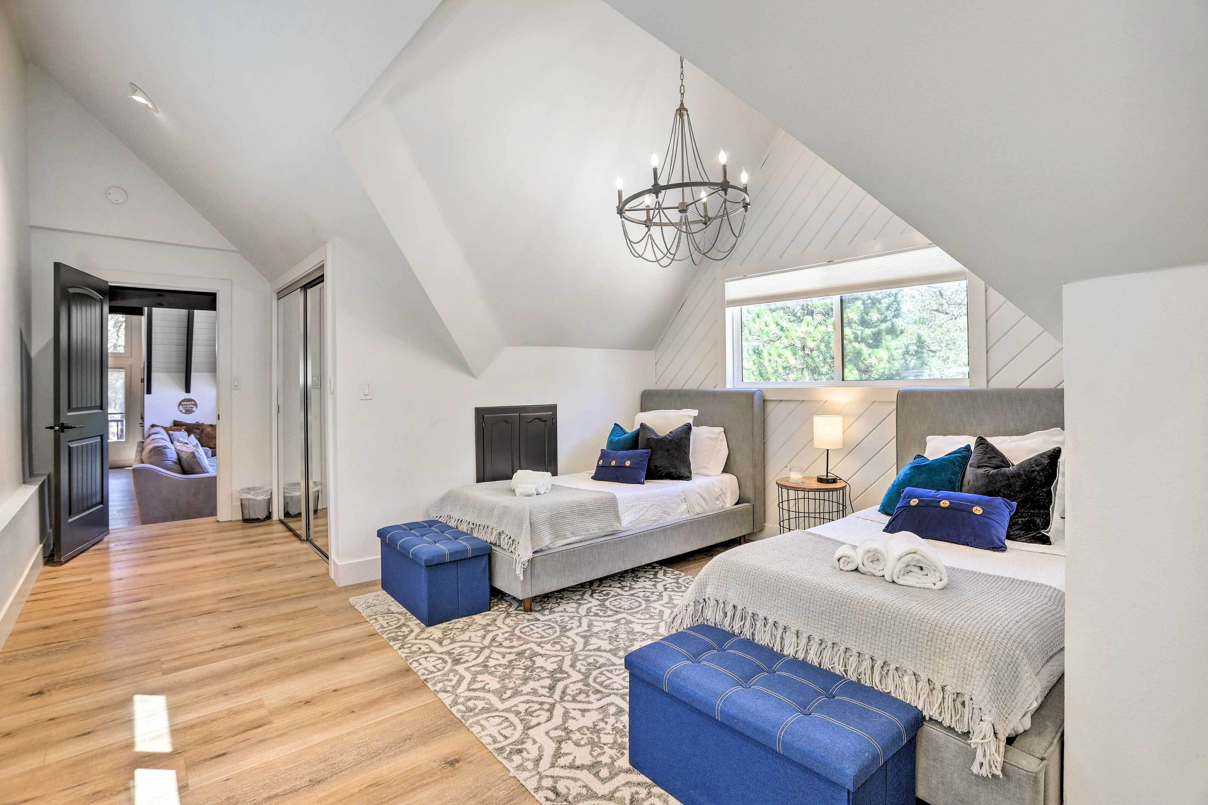A bedroom with two beds, a chandelier, and a large window.